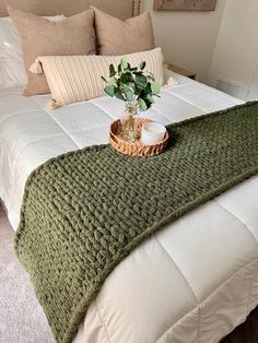 a bed with a green blanket on top of it and a potted plant in the middle