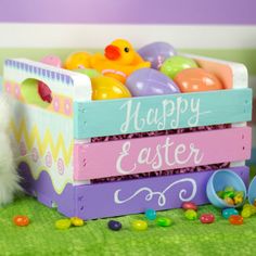 a small white rabbit sitting next to a wooden crate filled with easter eggs and colorful candies