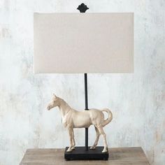 a white horse figurine sitting on top of a table next to a lamp