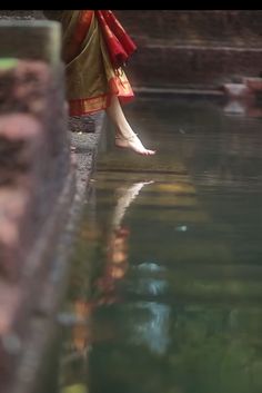 a woman standing on the edge of a body of water with her feet in the water