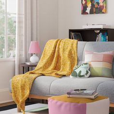 a living room with a gray couch covered in a yellow and pink blanket next to a window