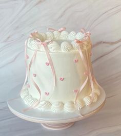 a white cake with pink ribbon and hearts on it, sitting on a platter