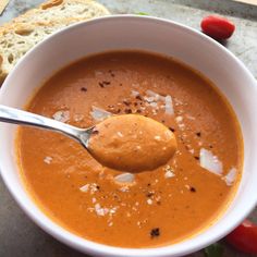 a bowl of soup with a spoon in it and bread on the table next to it