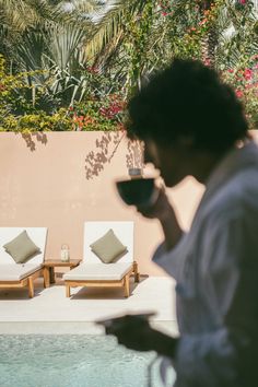 a man standing next to a swimming pool holding a cup of coffee in his hand