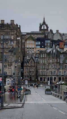 people are walking across the street in front of some very old buildings on a rainy day