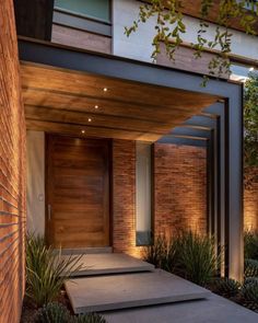 an entrance to a modern house with wooden doors and brick walls, surrounded by succulent plants