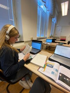 a woman sitting at a desk with laptops and books