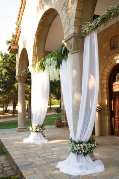 an outdoor wedding venue with white drapes and greenery on the columns, decorated with flowers