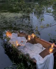 candles are lit in the middle of a row boat on water with flowers and greenery