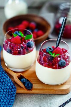 two glasses filled with yogurt and berries on a wooden tray next to spoons