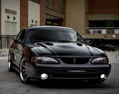 the front end of a black sports car parked in a parking lot next to a building