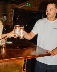 two people standing at a bar shaking hands with beer cans in front of the table