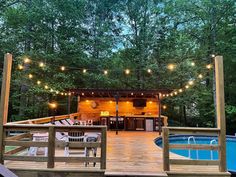 a deck with chairs and lights next to a swimming pool in the middle of a wooded area