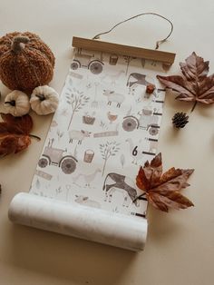 a table topped with fall leaves and pumpkins next to a piece of paper on top of a white surface