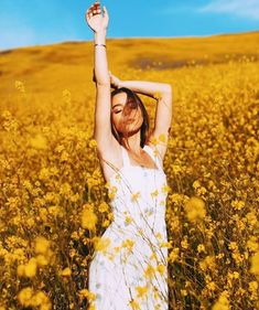 a woman standing in a field holding her arms up to the sky with yellow flowers