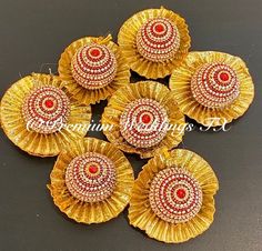 five gold and red flower shaped brooches on a black surface with white beads