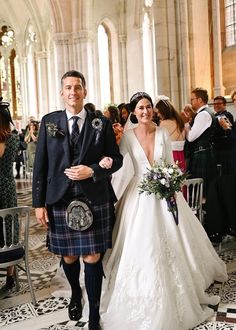 a man and woman in kilts walking down the aisle at a wedding ceremony together