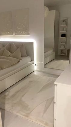 a white bed sitting in a bedroom next to a dresser and mirror with lights on it