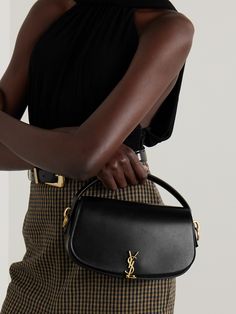 A practical investment piece, SAINT LAURENT's Italian-made 'Voltaire’ tote is crafted from buttery smooth black leather and punctuated with a signature gold-tone logo plaque. It has a short top handle and optional shoulder strap, which you can adjust to a comfortable drop. The compact, structured design is ideal for holding your phone, cardholder and lip gloss. Ysl Hat Outfit, Black Purse Designer, Ysl Bags, Yves Saint Laurent Bag, Ysl Handbags, Saint Laurent Tote, Gucci Eyewear, Yves Saint Laurent Bags