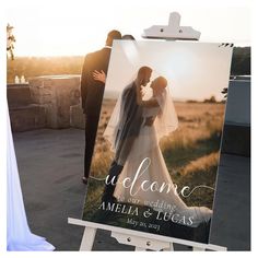 a welcome sign with a bride and groom kissing in front of the sun at their wedding