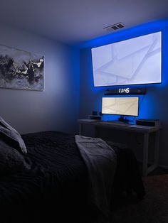 a bedroom with a bed, desk and large screen tv on the wall above it