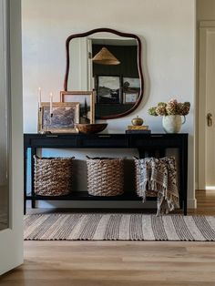 a console table with baskets on it and a large mirror above it, in front of a doorway