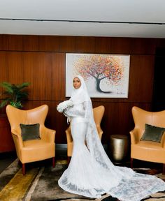 a woman in a white wedding dress standing next to two chairs and a painting on the wall