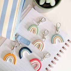 several rainbow shaped key chains sitting on top of a notepad next to a cup