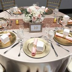 the table is set with gold plates, silverware and pink napkins