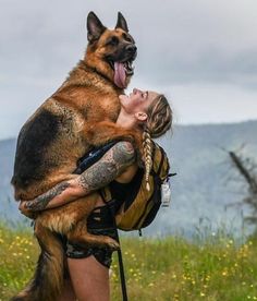 a woman holding a large dog on her back in the middle of a grassy field