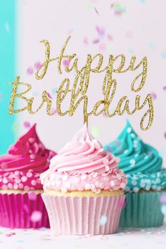 three cupcakes with pink, blue and green frosting in front of a happy birthday sign