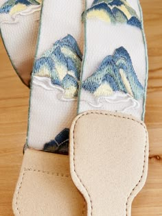 a pair of blue and yellow mountain print guitar straps on a wooden surface with white stitching