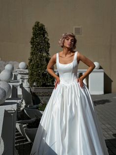 a woman in a white wedding dress standing on a brick walkway with her hands on her hips