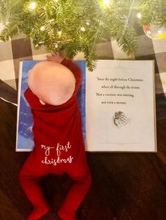 a baby is laying down next to a christmas tree with a card in front of it