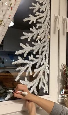 a person is using a remote control to paint a window with white leaves on it