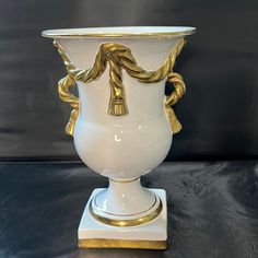 a large white vase with gold decoration on it's sides, sitting on a black surface