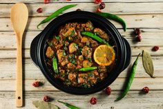 a bowl filled with meat and vegetables next to a wooden spoon on top of a table