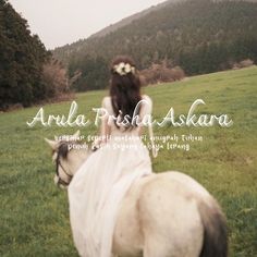 a woman riding on the back of a white horse in a lush green field next to a forest