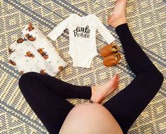 a woman laying on top of a bed next to two baby onesuits and shoes