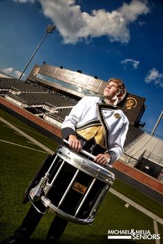 a man in uniform holding a drum on a football field with an empty bleachers behind him