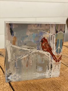 a glass block with a bird painted on it sitting on top of a wooden table