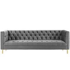 a gray velvet couch with gold legs and buttons on the back, against a white background