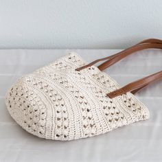 a white crocheted bag sitting on top of a bed next to a wall