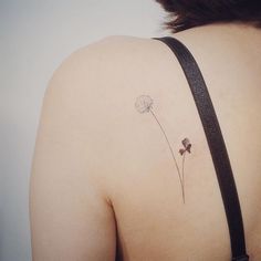 the back of a woman's shoulder with a dandelion tattoo on it