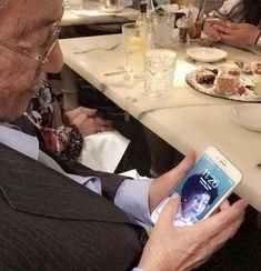 an older man sitting at a table looking at his cell phone