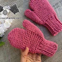 two pink knitted mittens sitting on top of a wooden table next to white flowers