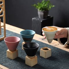 a person holding a coffee cup in front of four cups on small wooden blocks,