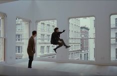 two people standing in an empty room with open windows and one person jumping into the air