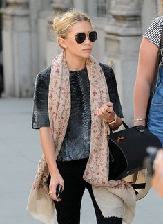 a woman walking down the street carrying a black purse and wearing sunglasses with a scarf around her neck