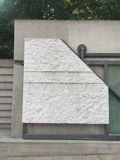 a white monument with writing on it next to a wall and trees in the background